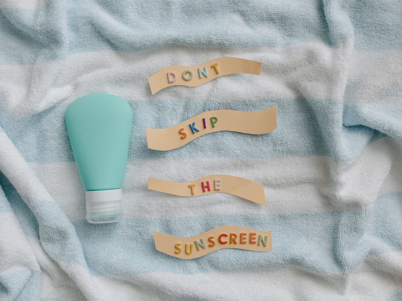 A sunscreen bottle on a striped towel beside letters spelling 'don't skip the sunscreen'