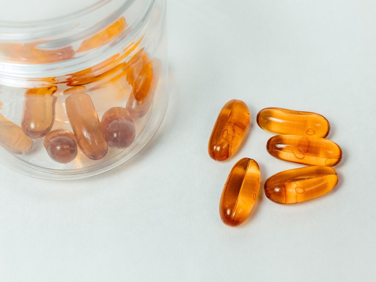 Amber softgel capsules spilling out of a glass jar onto a white surface