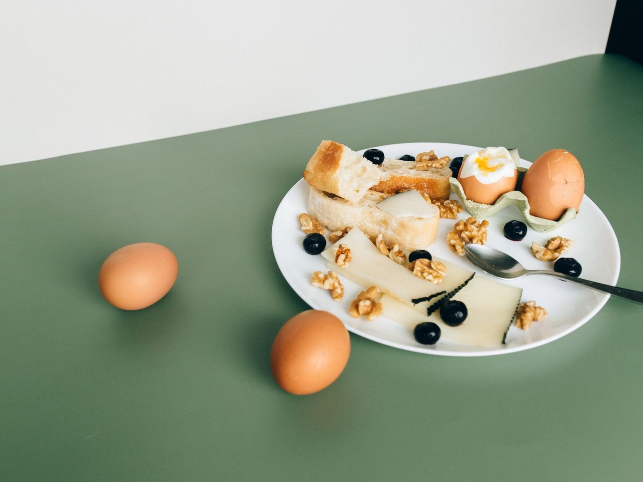 A plate of boiled eggs, cheese, walnuts and blueberries on a green table