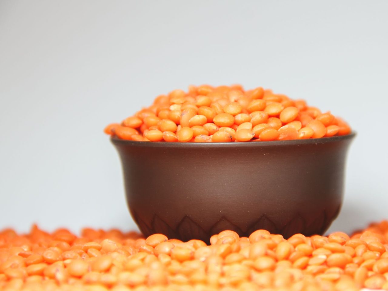 A brown bowl overflowing with red lentils