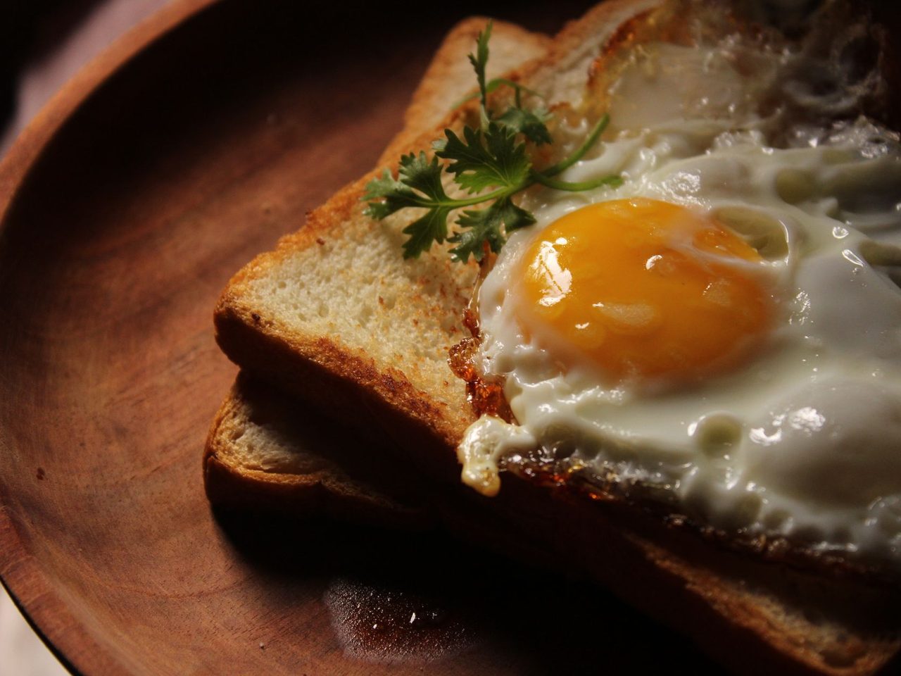 A fried egg on toast with fresh greens on a wooden plate