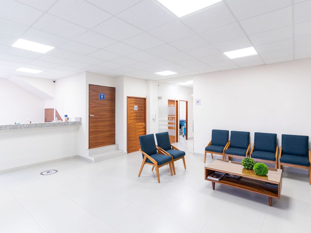 A bright, empty clinic waiting room with blue chairs