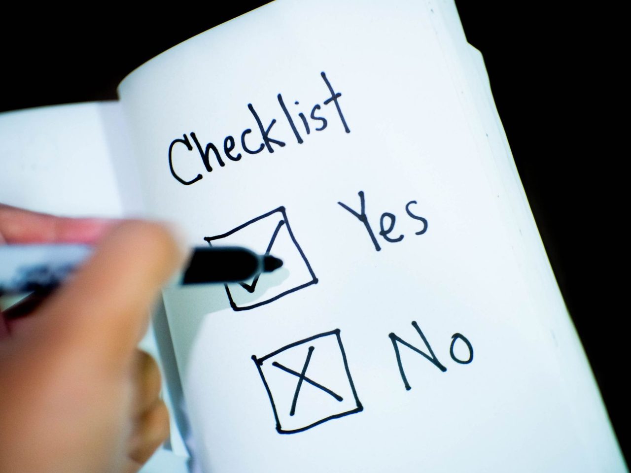 A hand ticking a checklist written in a notebook, with yes and no boxes