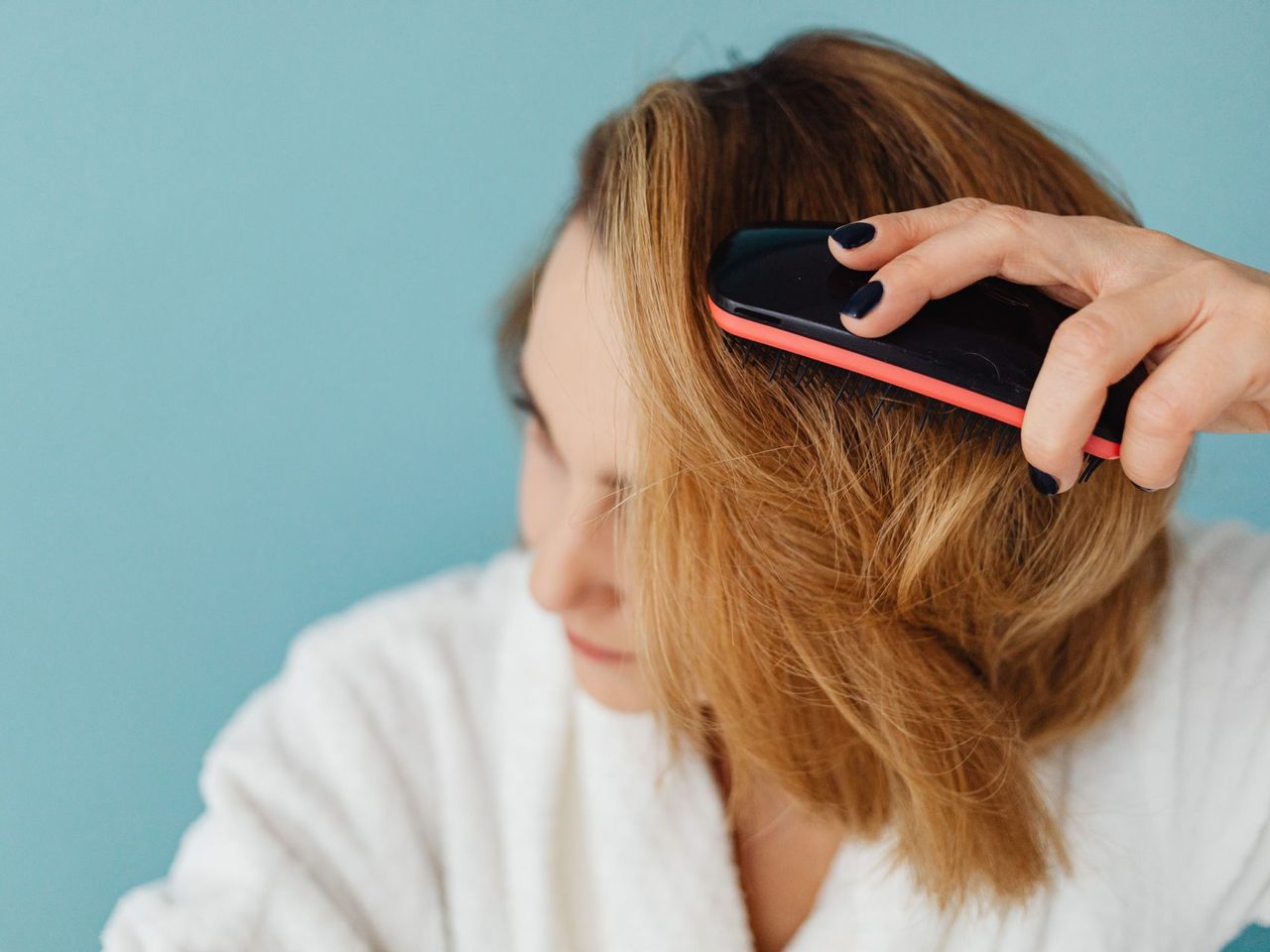 A woman in a white bathrobe brushing her long brown hair with a paddle brush