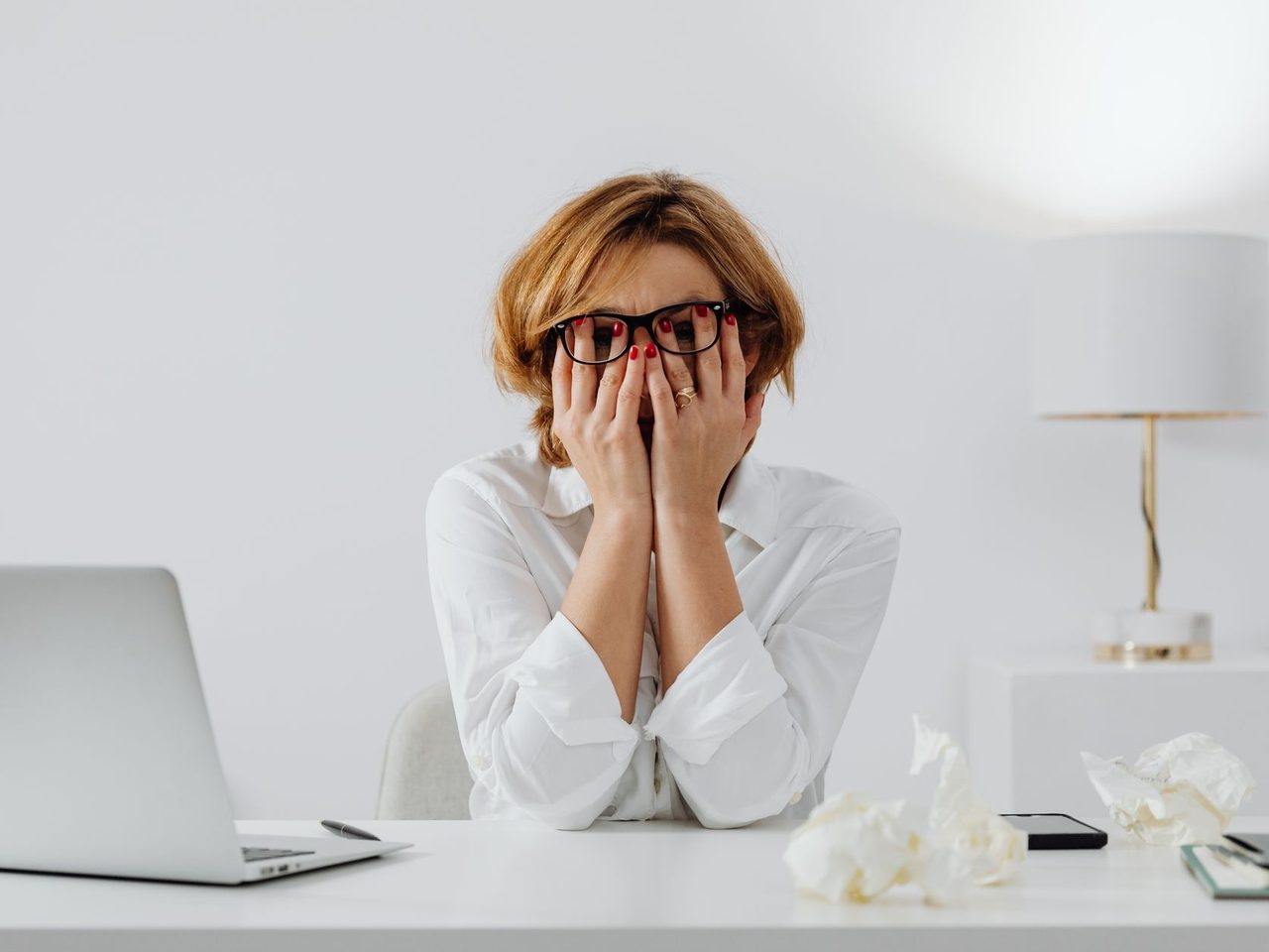 A woman sitting at a desk with a laptop, covering her face with her hands