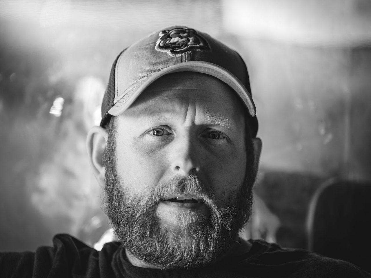 Black and white portrait of a bearded man wearing a baseball cap