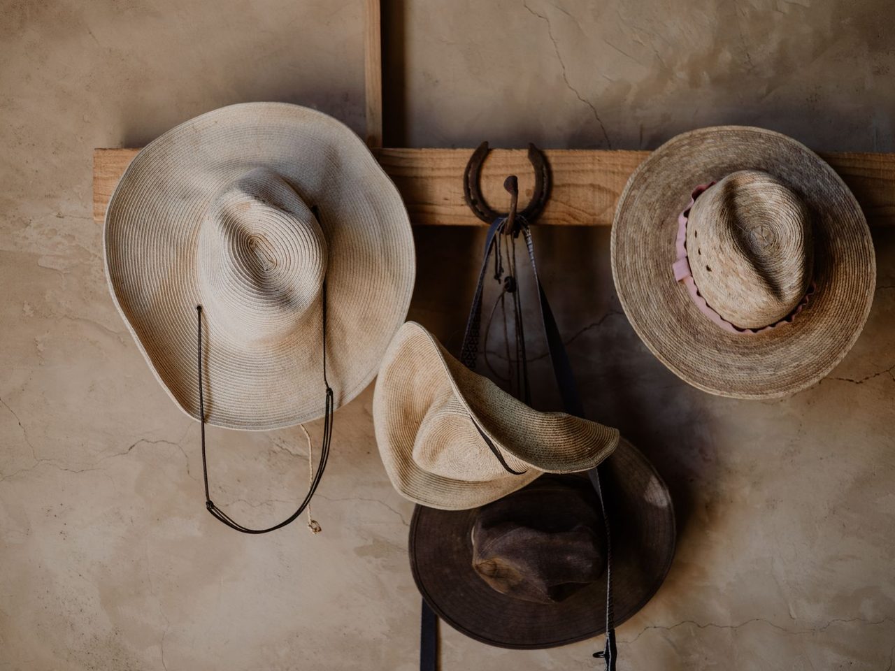 Several woven and felt hats hanging from hooks on a rough plaster wall