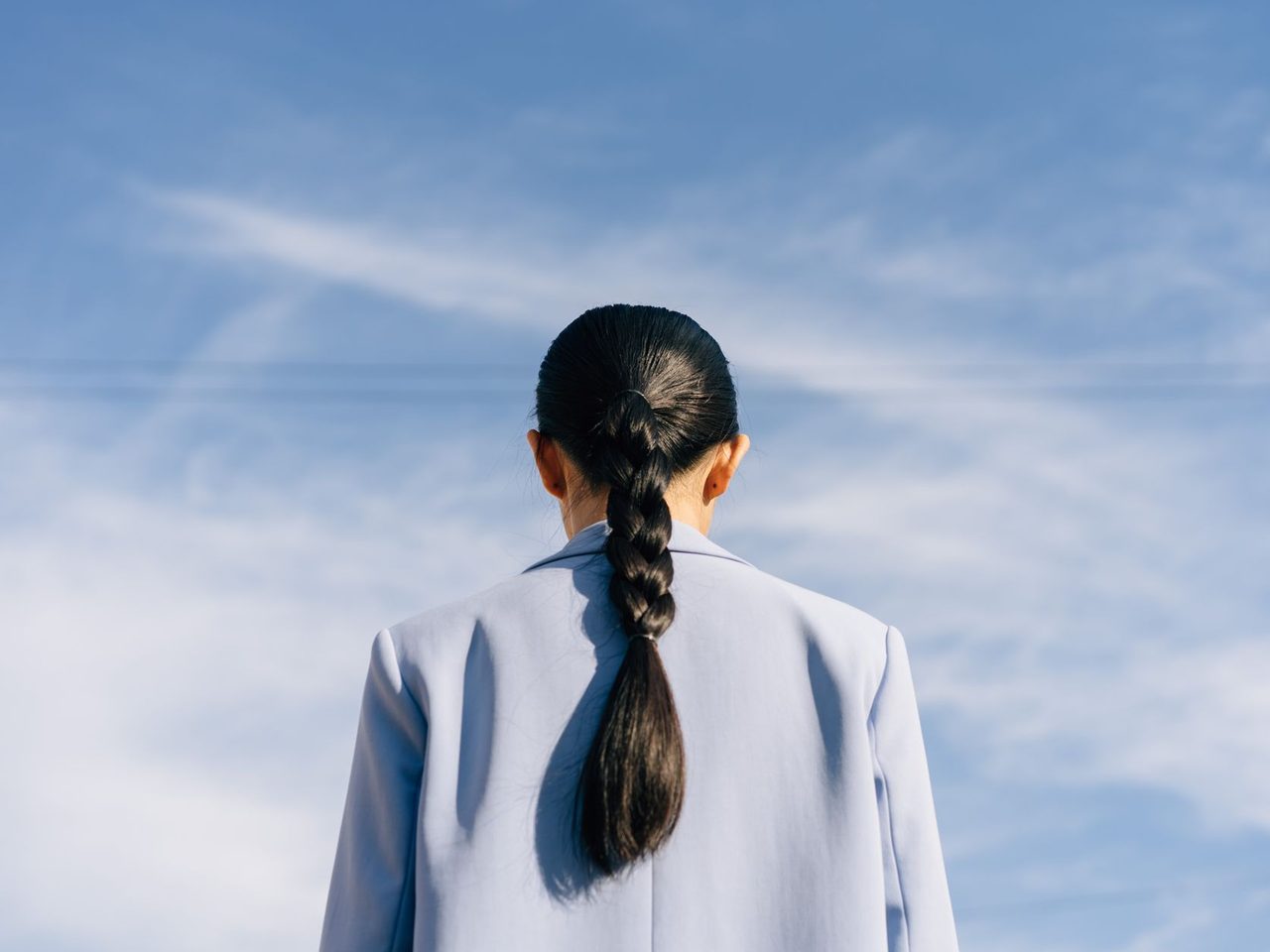 A woman seen from behind with her dark hair in a long braid against a blue sky