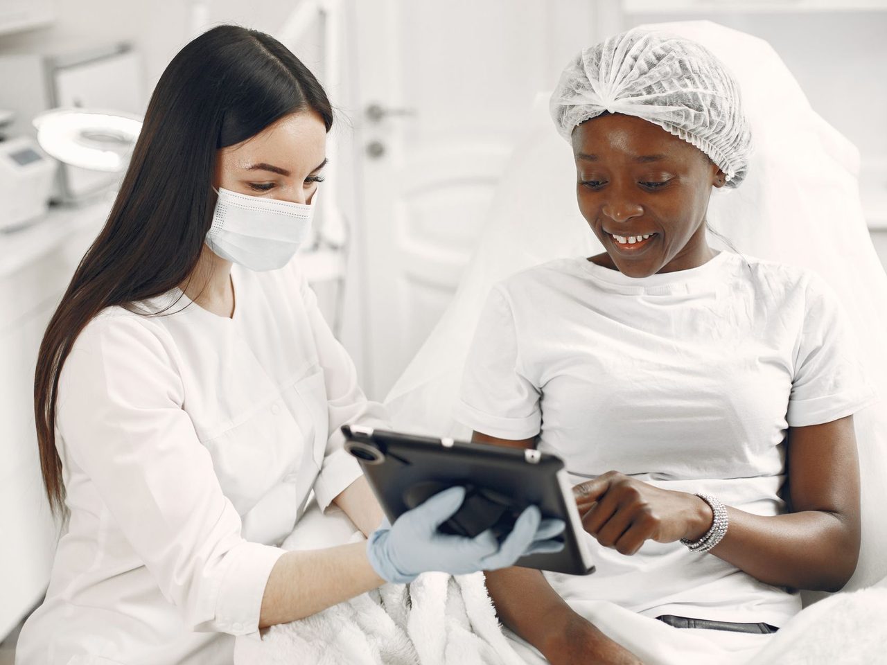 A smiling patient and a dermatologist in white looking at a tablet together in a clinic