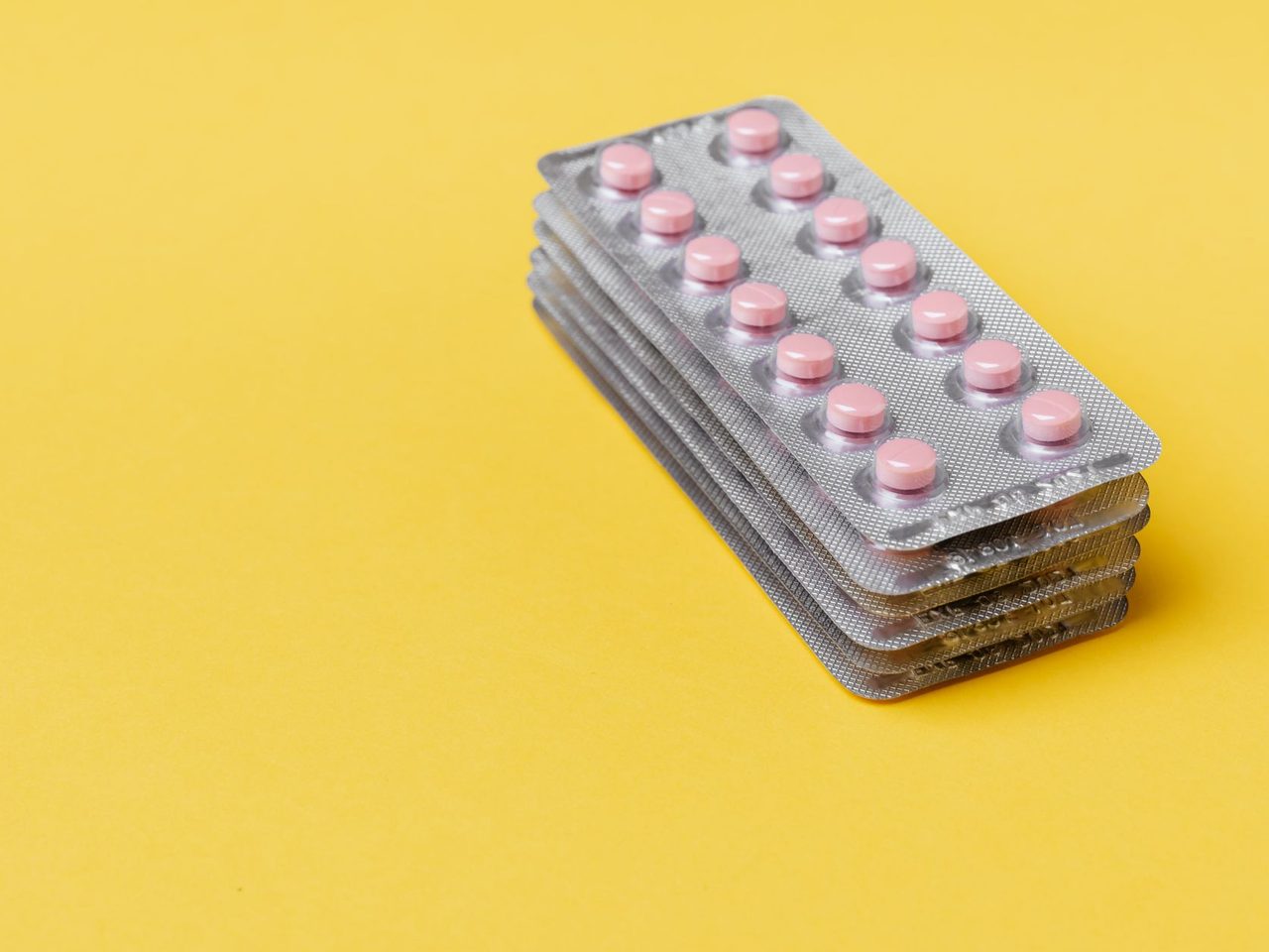 Stacked blister packs of small round pink pills on a yellow background