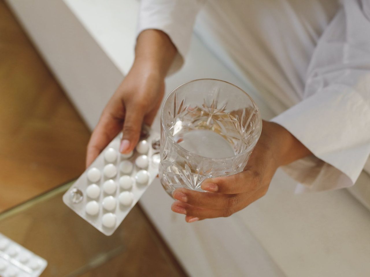 Close-up of hands holding a blister pack of pills and a glass of water