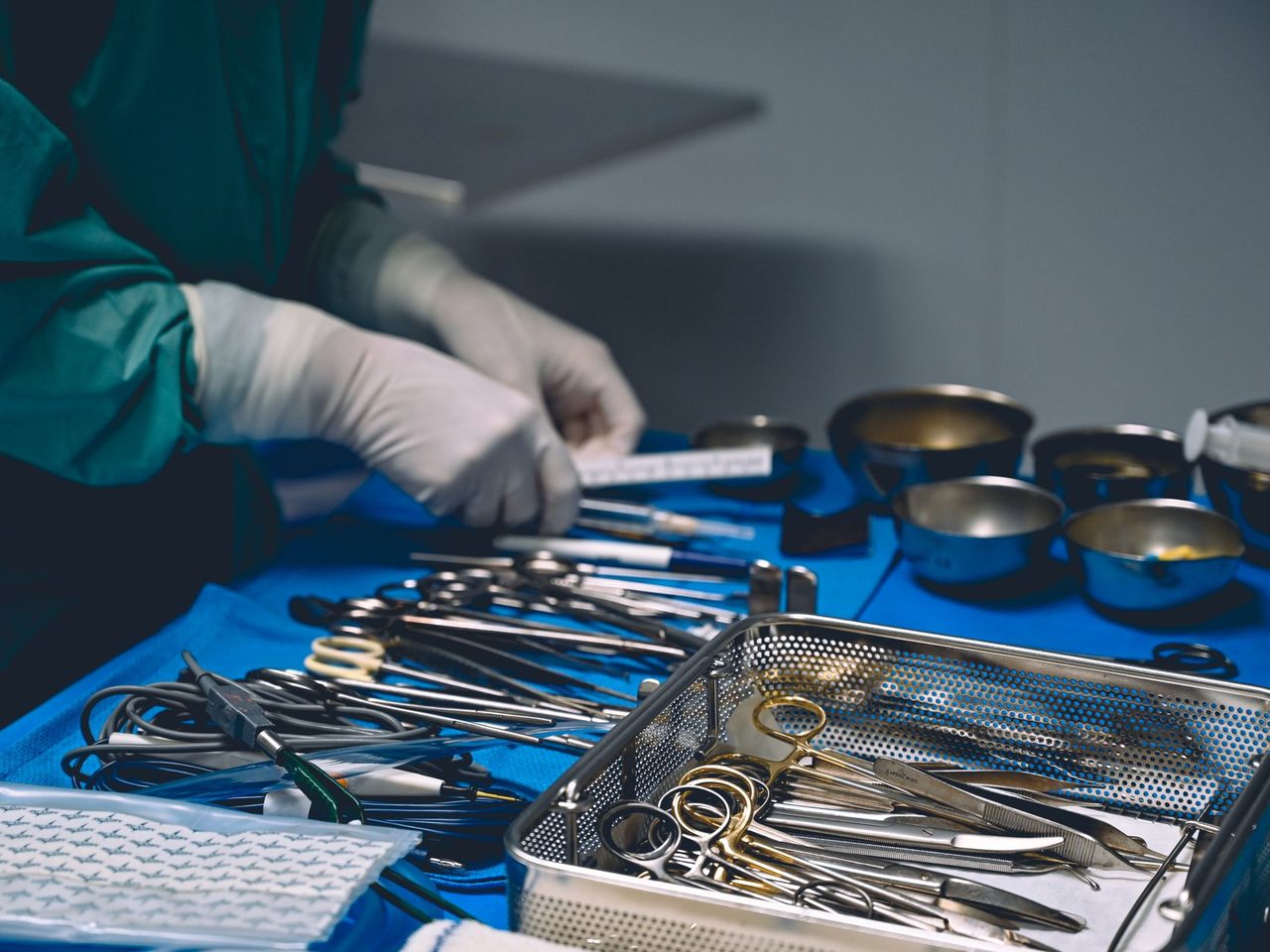 A healthcare worker in gloves setting out surgical instruments on a blue sterile table