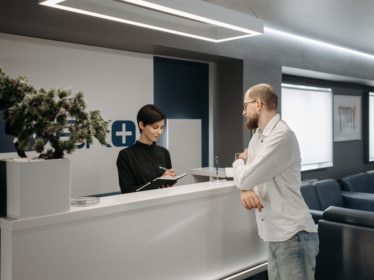 A man talking with a receptionist at the front desk of a modern clinic