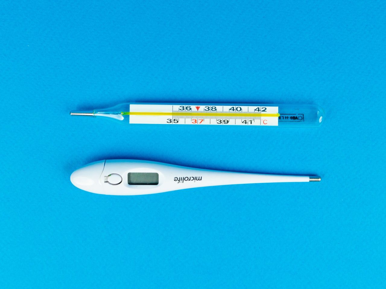 A digital thermometer and a glass thermometer on a bright blue background
