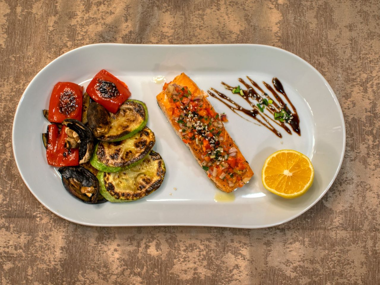 Grilled salmon with roasted vegetables and a lemon slice on a white plate