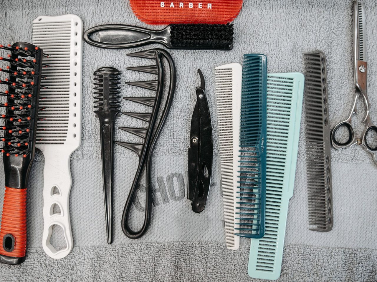 Flat lay of assorted combs, a round brush, clips and scissors on a gray surface