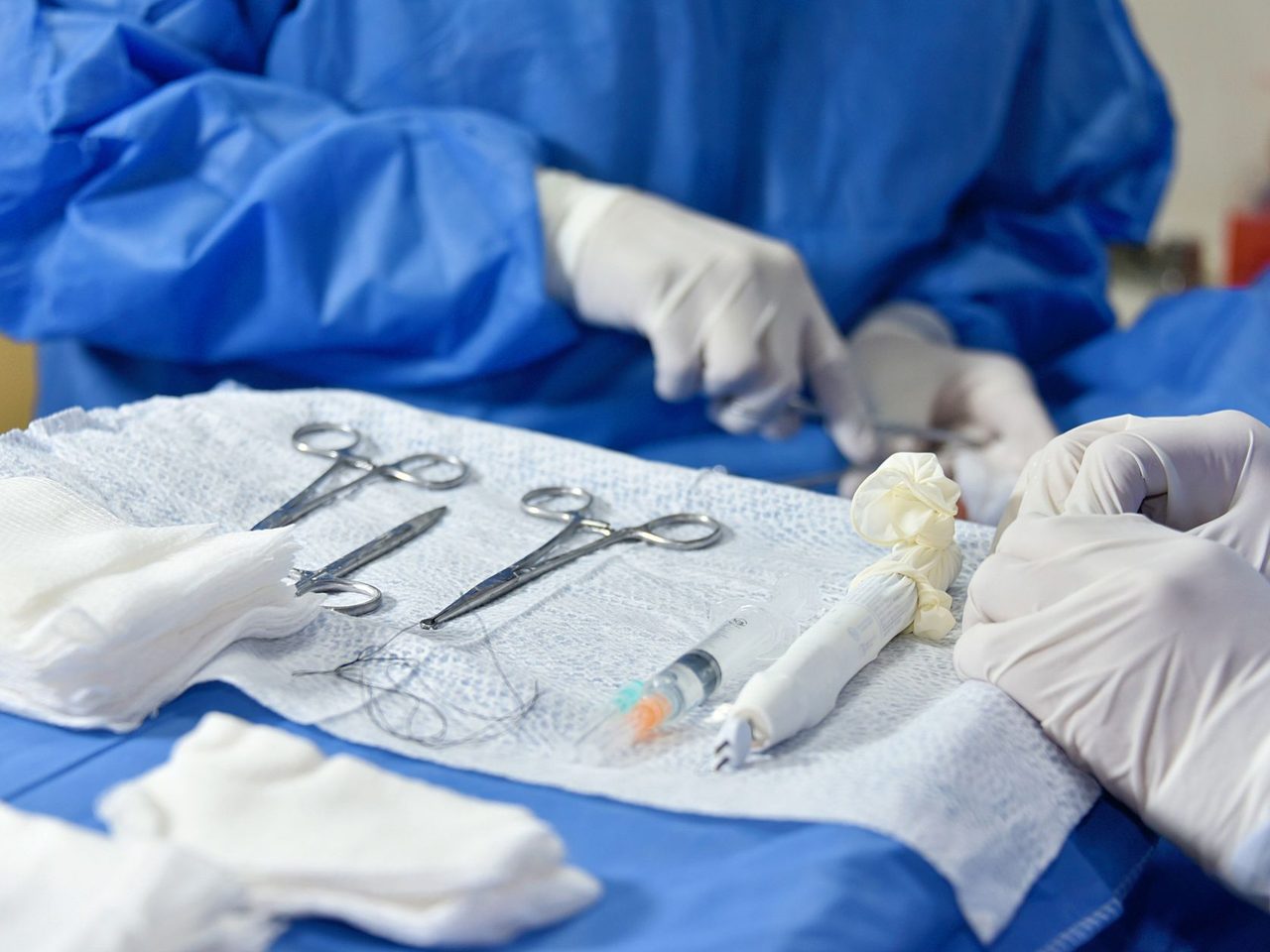 Gloved hands near a set of surgical instruments arranged on a blue drape