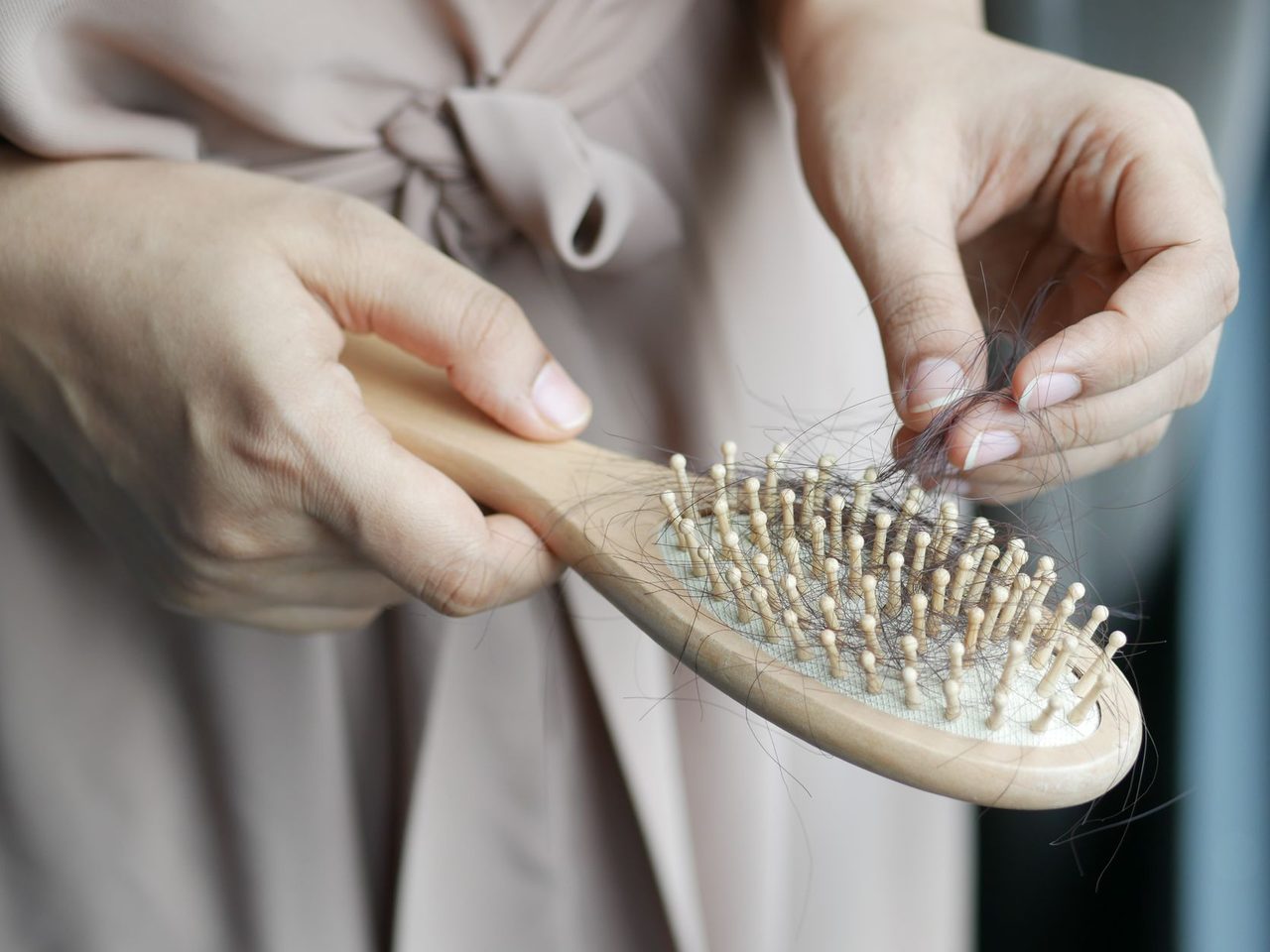 Hands pulling loose hairs out of the bristles of a wooden paddle brush