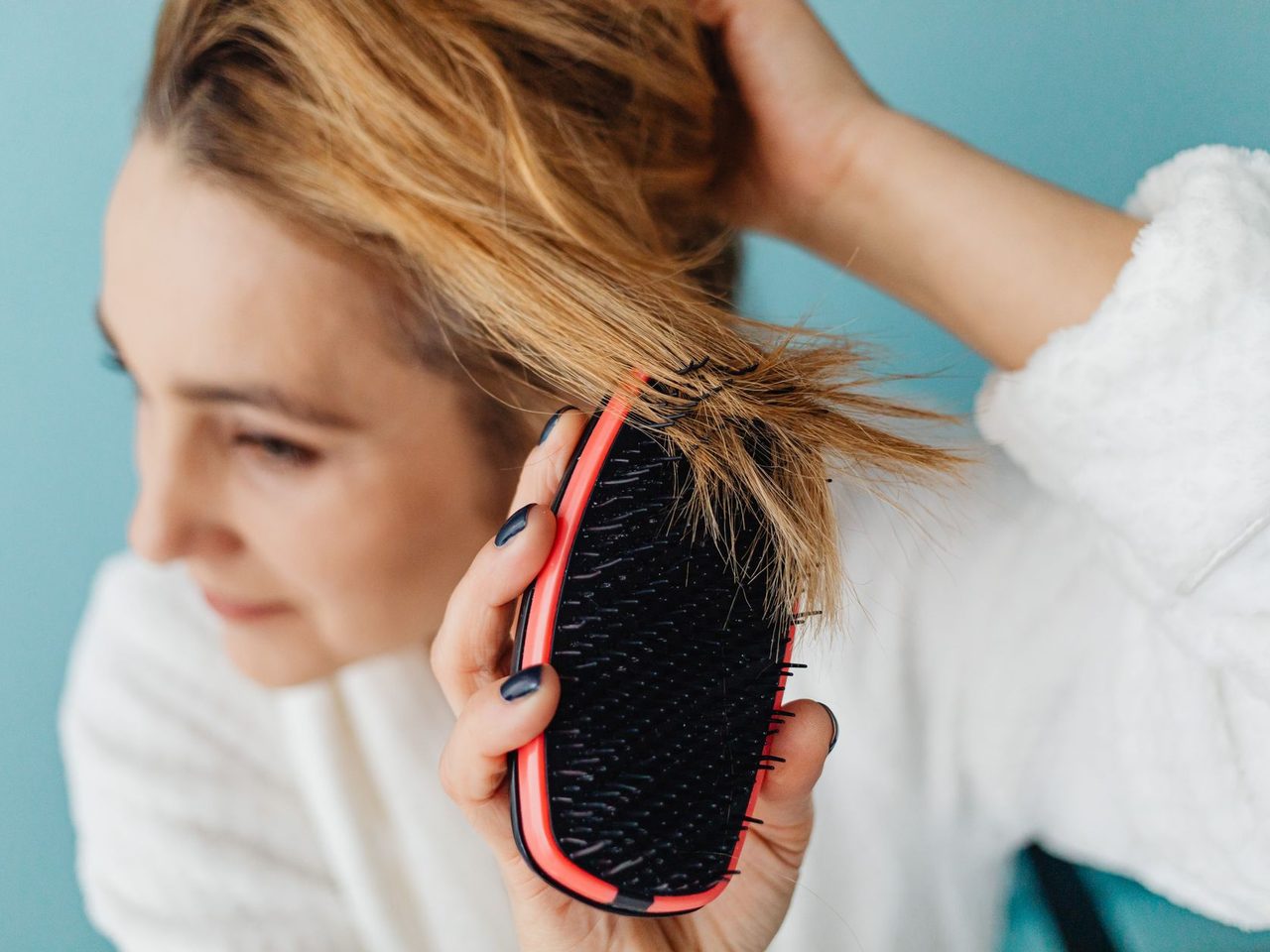 A woman with blonde hair brushing it with a red and black paddle brush