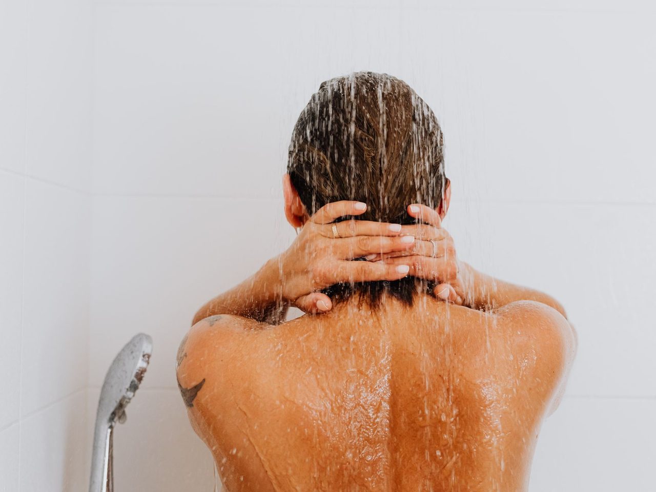 A person seen from behind rinsing their hair under a shower