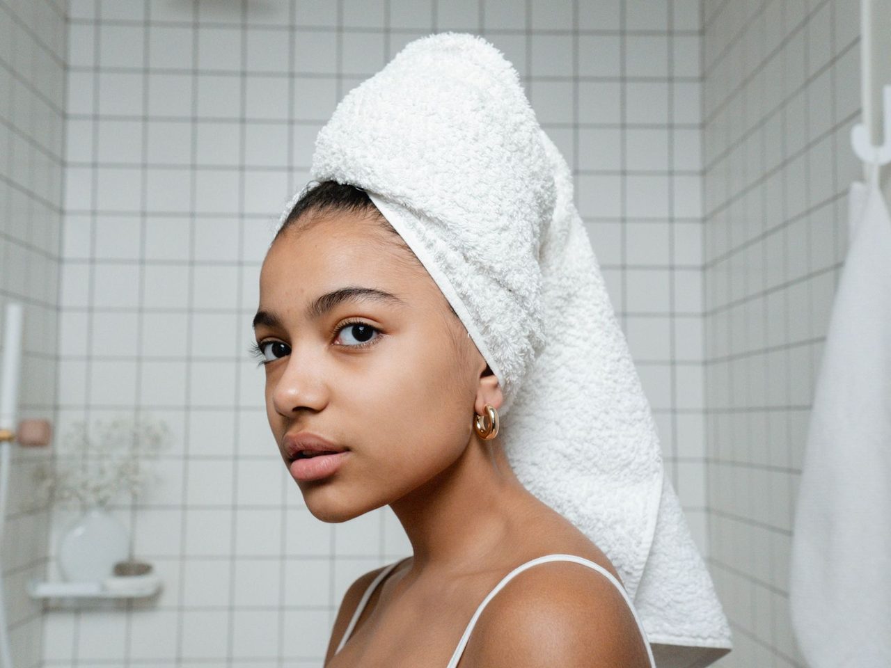A young woman with her hair wrapped in a white towel in a tiled bathroom