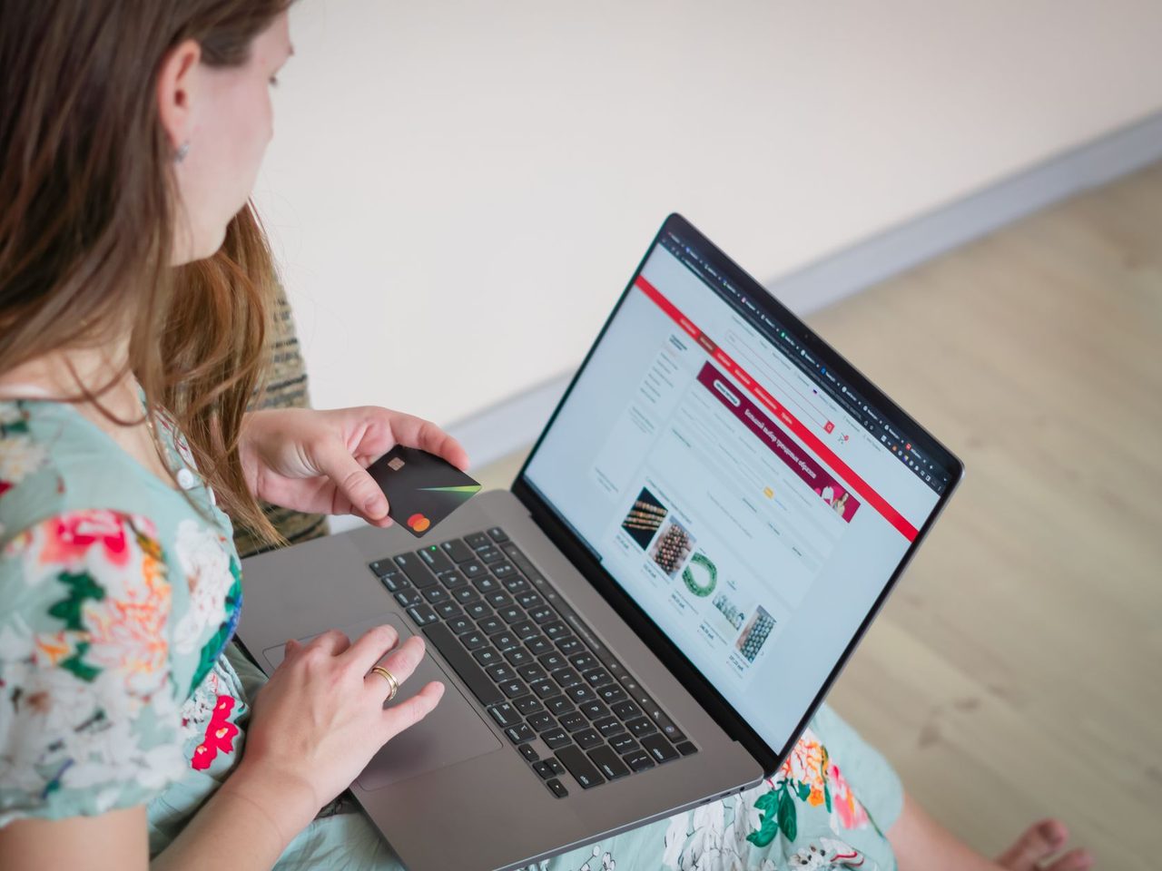 A woman in a floral dress looking at a shopping website on a laptop