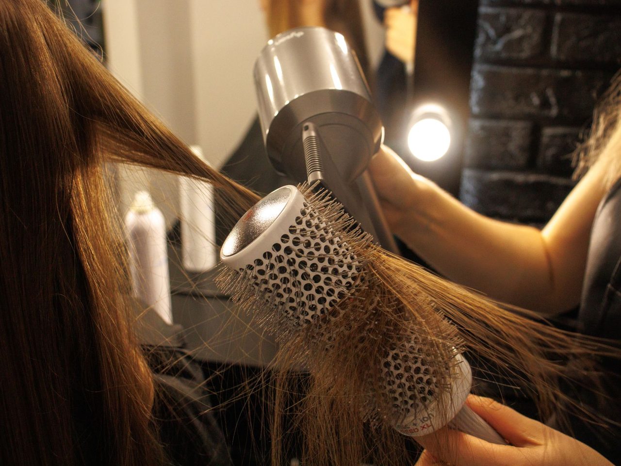 Close-up of a stylist drying long hair with a round brush and a hair dryer