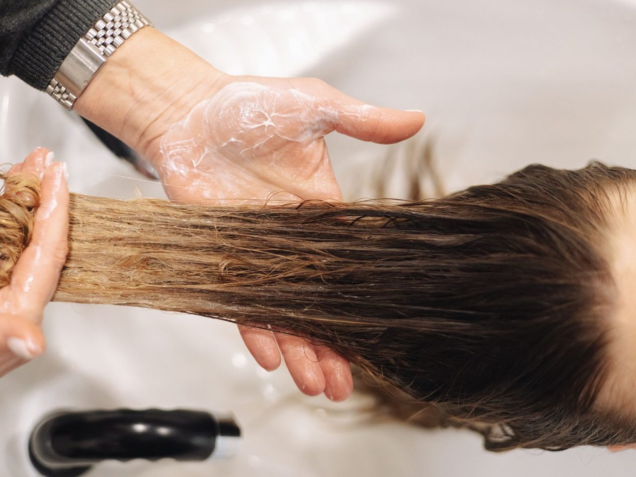 Close-up of a hair washer's hands rinsing long hair at a salon basin