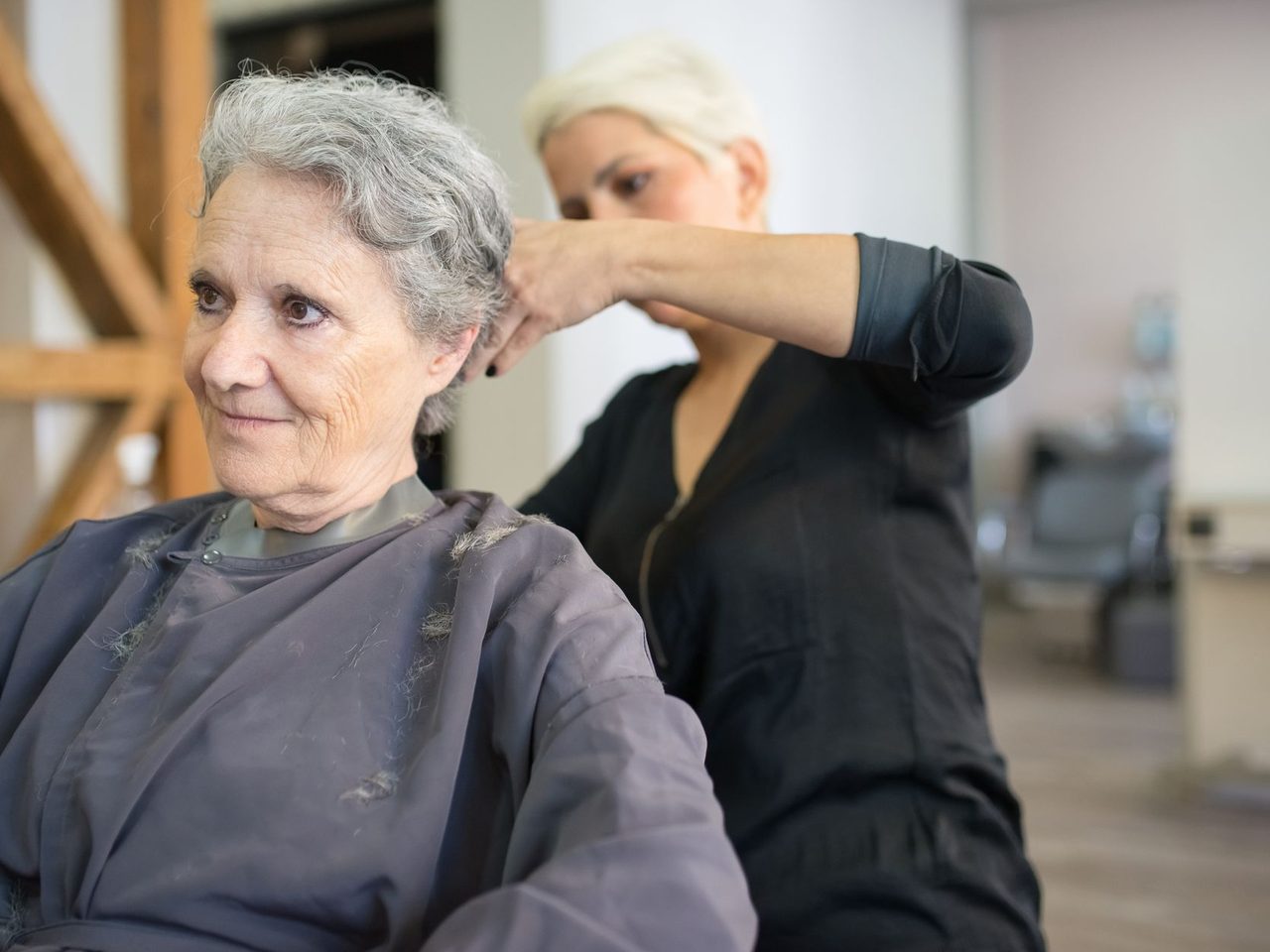An older woman with short gray hair sitting in a salon chair while a stylist cuts it