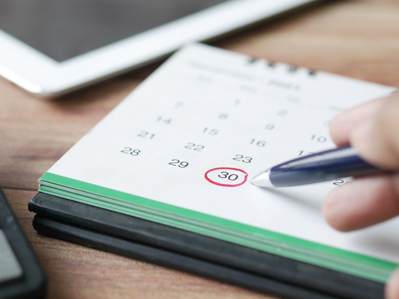 A hand circling a date on a desk calendar with a pen