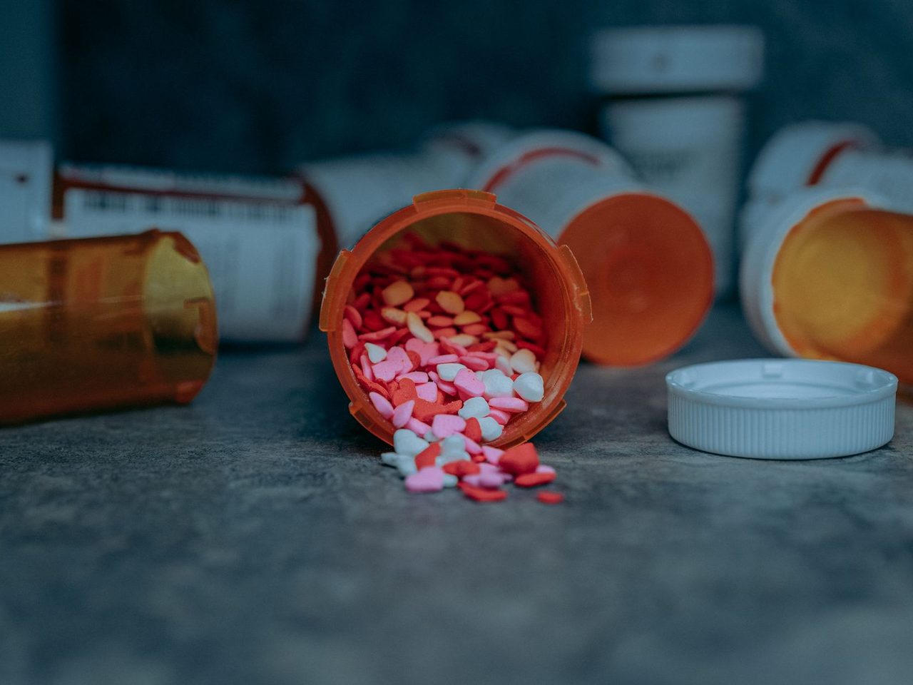 Colorful pills spilling out of an orange prescription bottle onto a counter