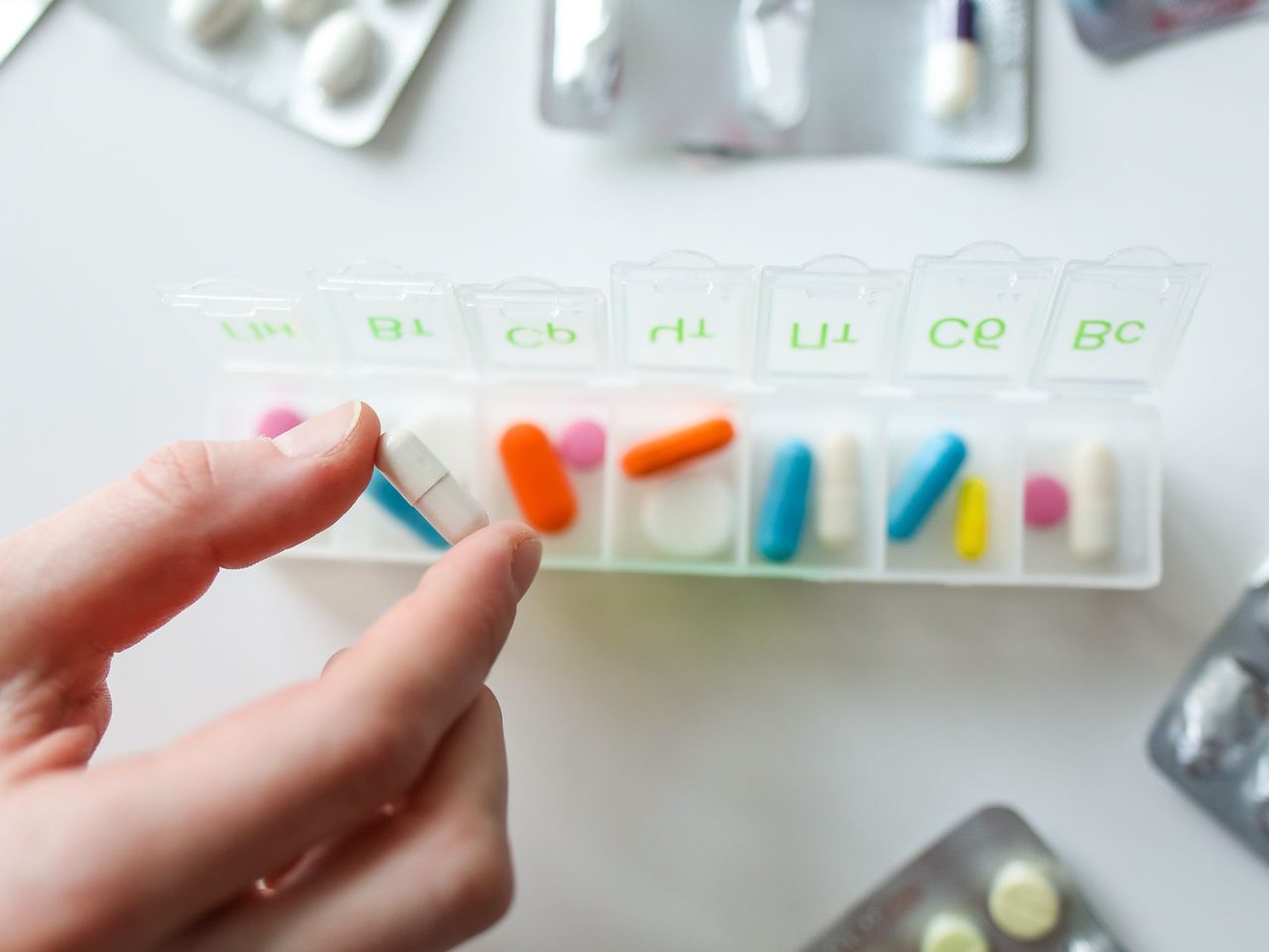 A hand taking a capsule from a clear weekly pill organizer