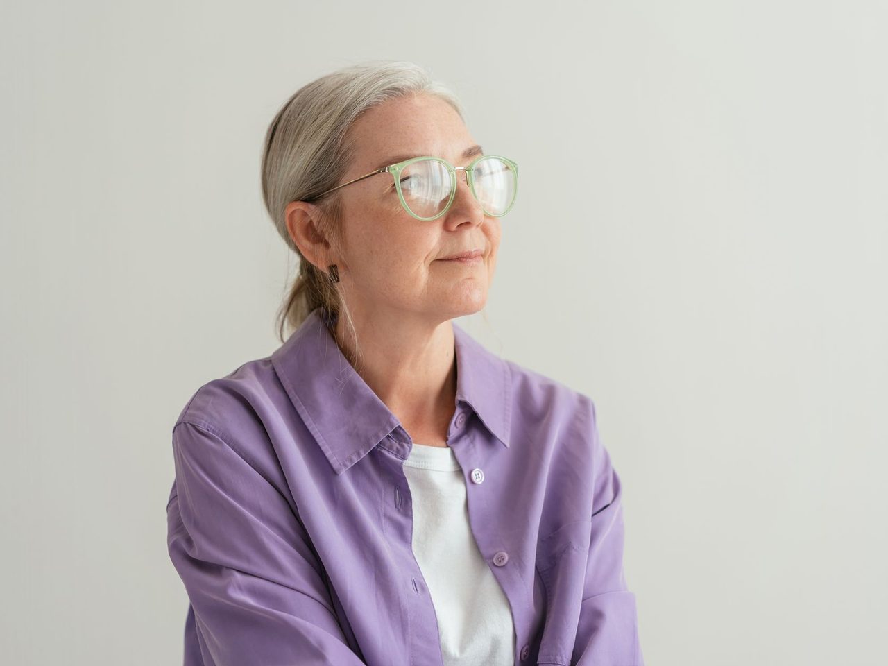 An older woman with gray hair tied back, wearing glasses and a purple shirt