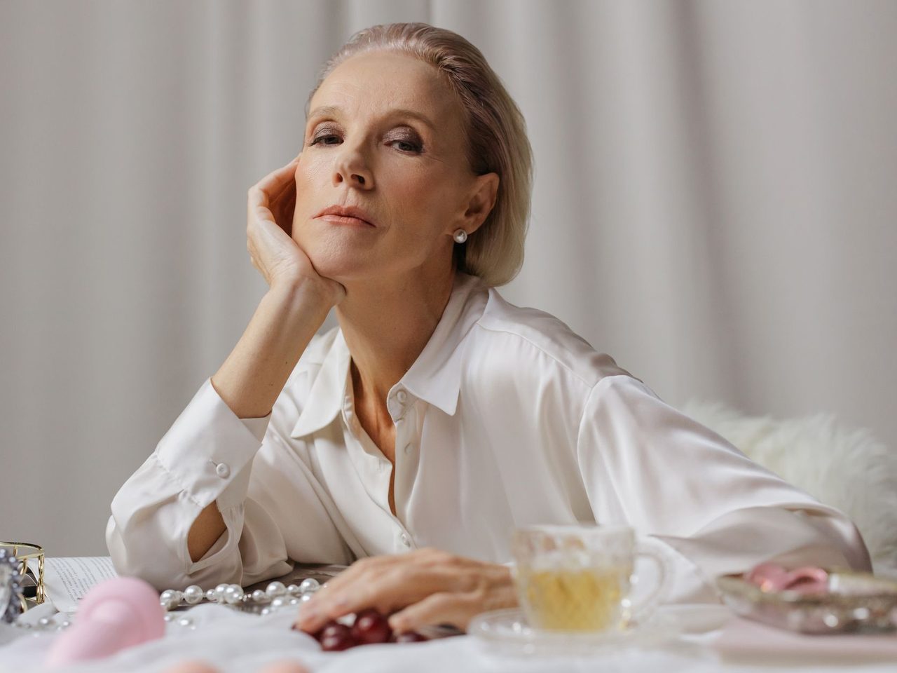 A woman with short swept-back blonde hair in a white shirt leaning on a table