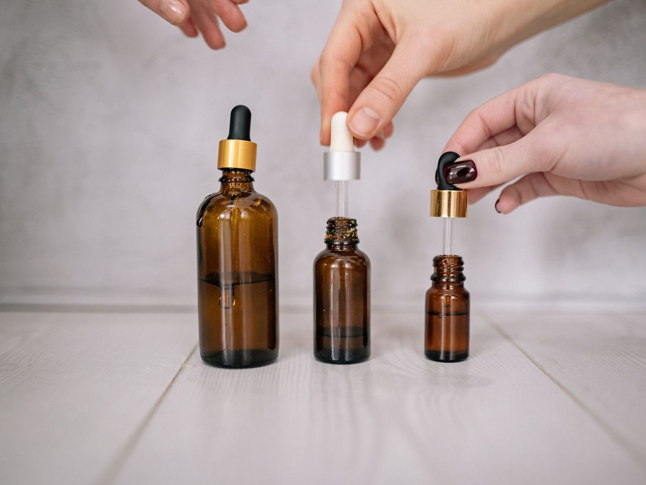Hands lifting droppers from three small brown glass bottles