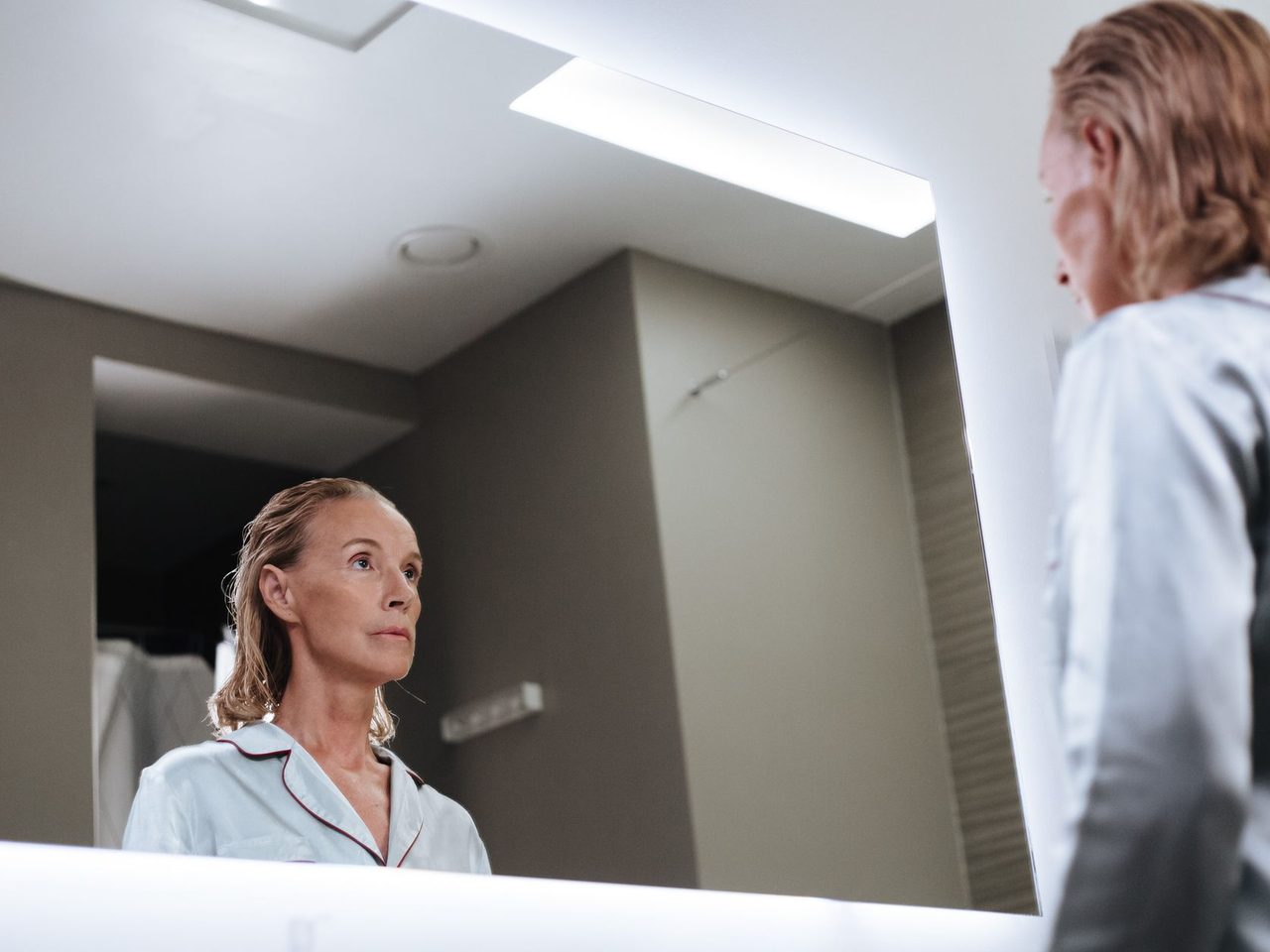 An older woman looking at herself in a bathroom mirror