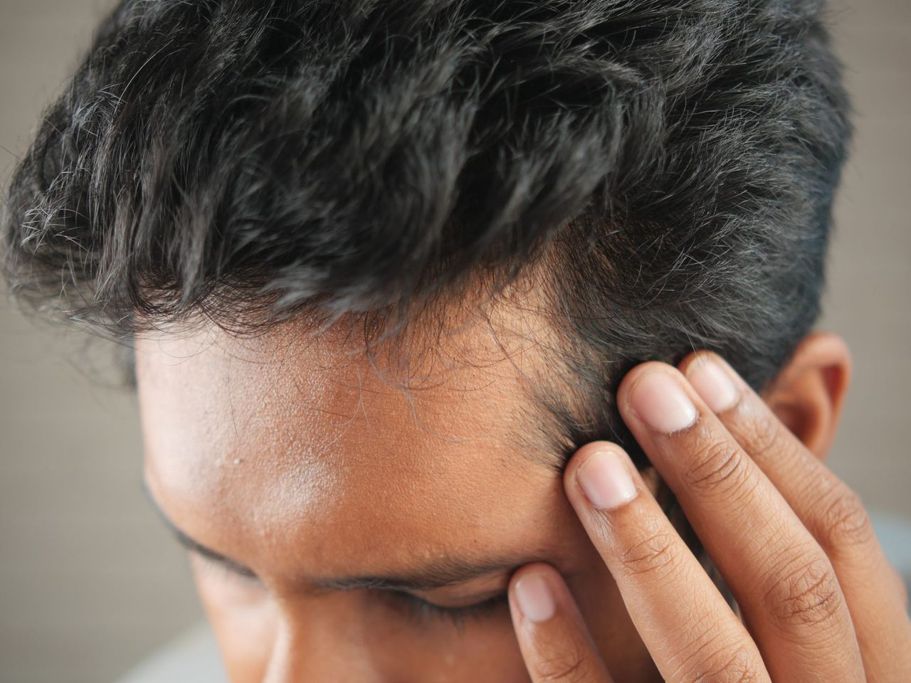 Close-up of a man's fingers resting against the dark hair at the side of his head