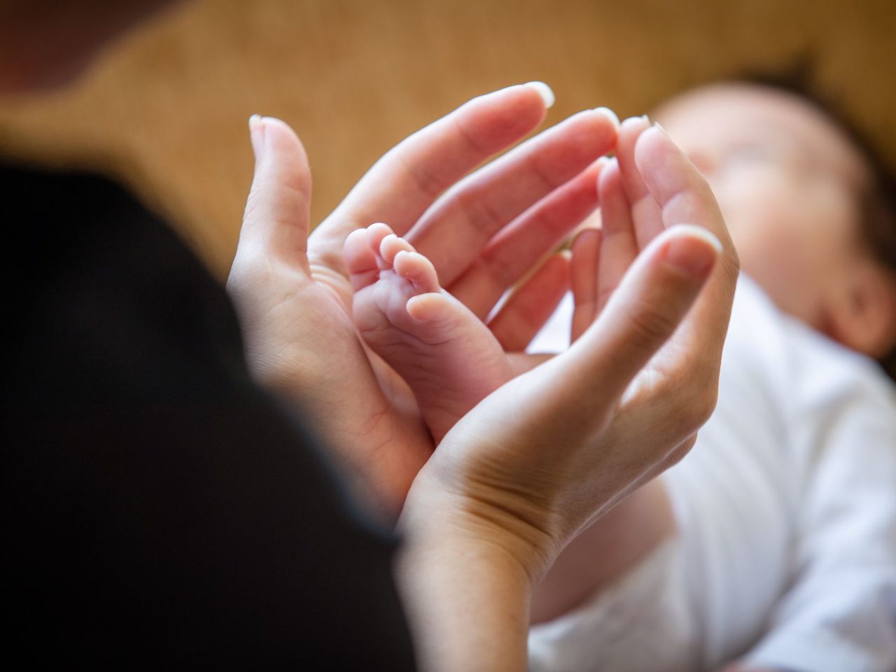 Close-up of a parent's hands gently holding a newborn baby's tiny feet