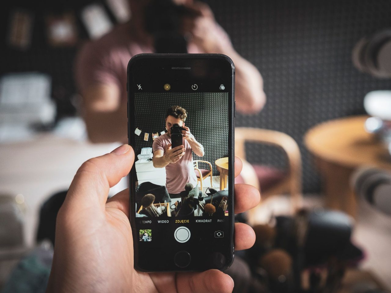 A hand holding a phone showing a mirror selfie on its screen