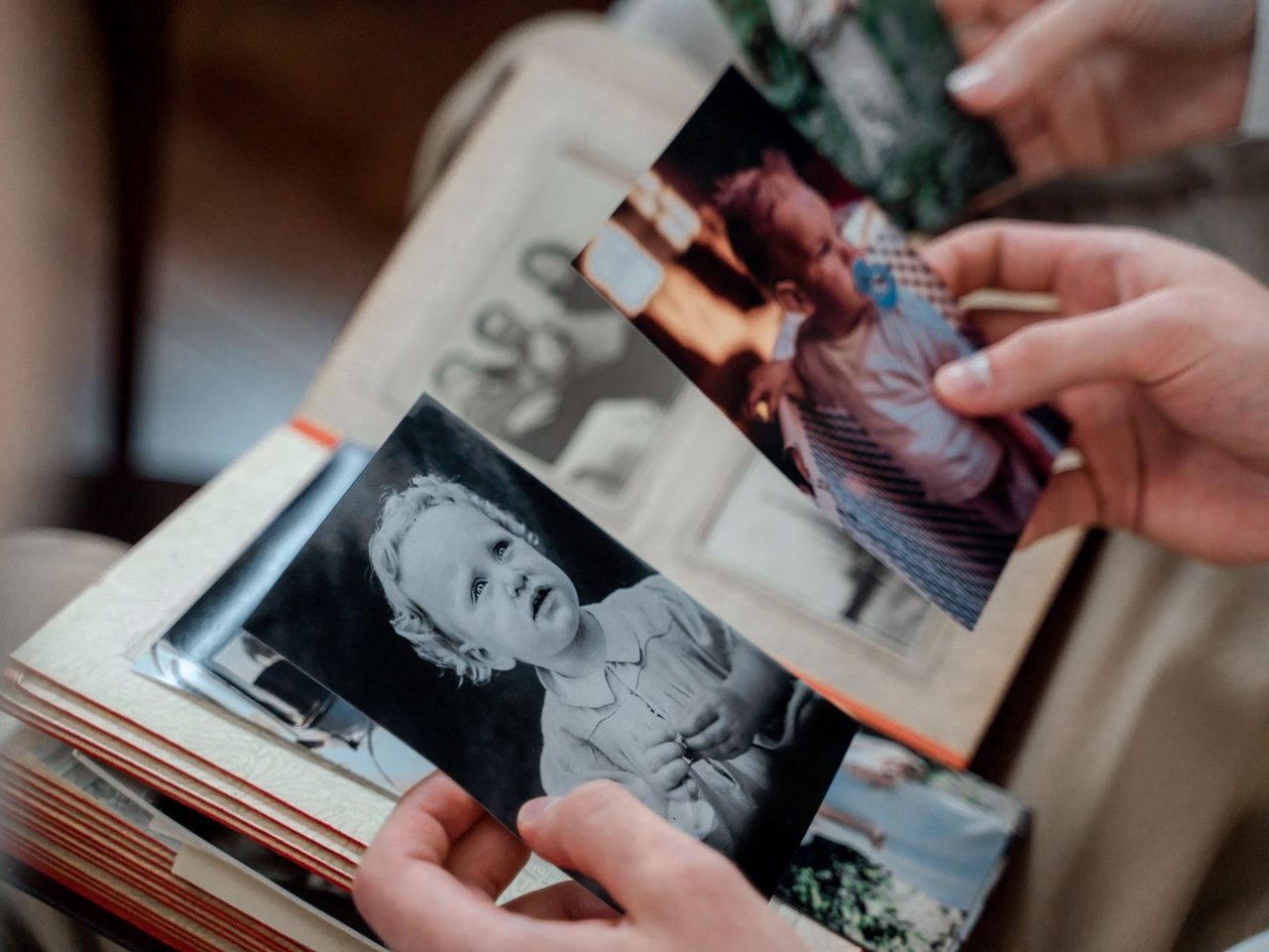 Hands holding old black and white family photographs over an open album