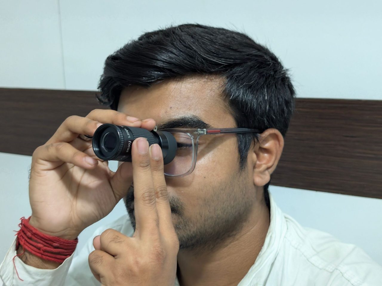 A man looking through a small handheld dermatoscope