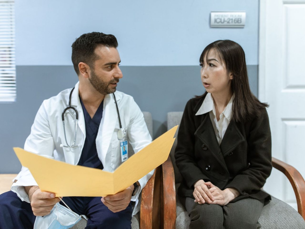 A doctor holding a folder talking with a woman patient seated across from him