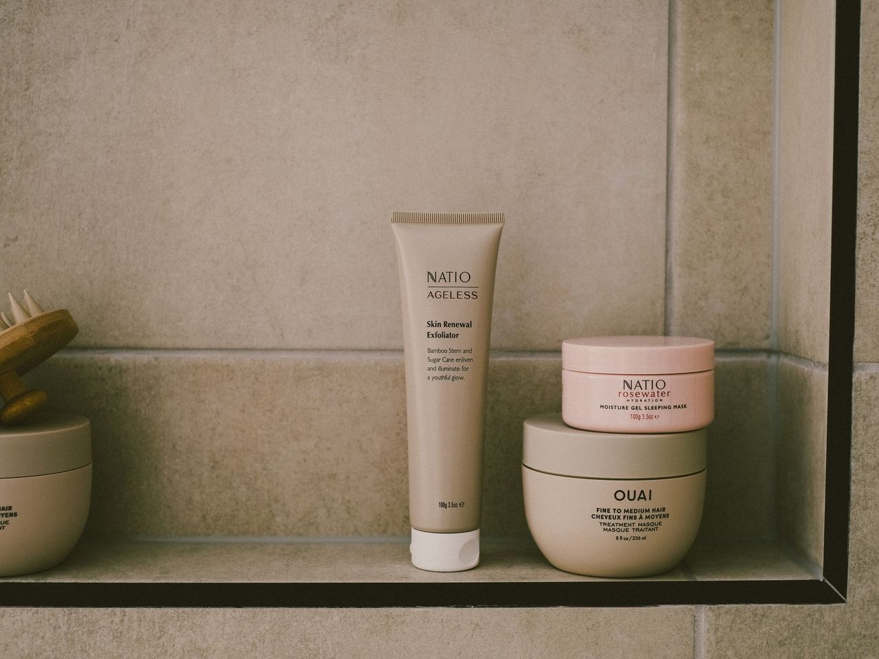 A tube and two jars of skin care products on a bathroom shelf in beige tones