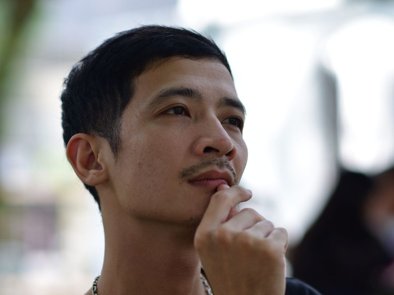A thoughtful young man resting his chin on his hand outdoors