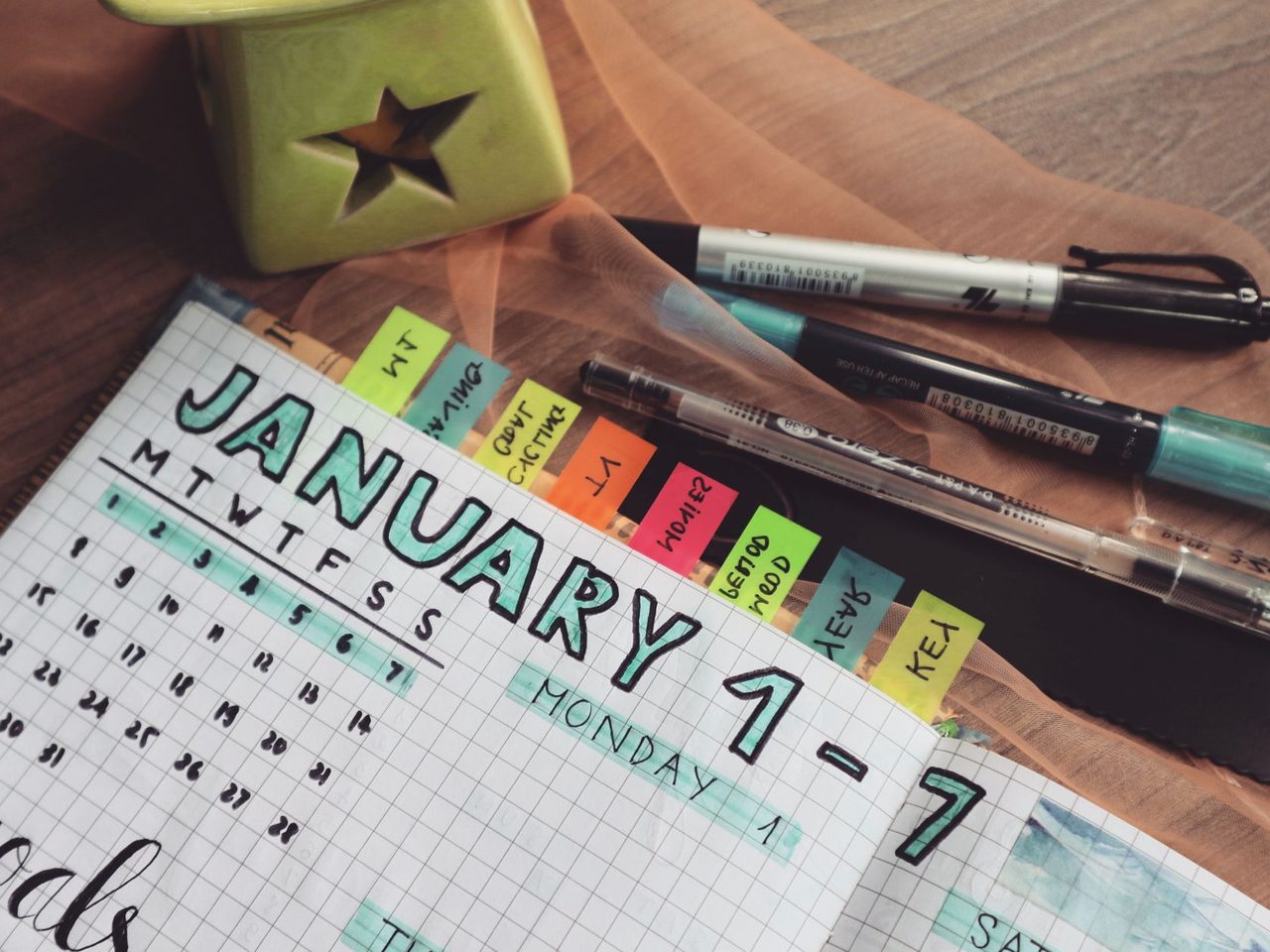 A planner open on a desk with colored tabs, pens and the week's dates