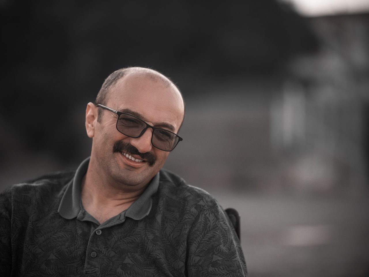 Portrait of a smiling man with short receding hair and glasses in a gray polo shirt