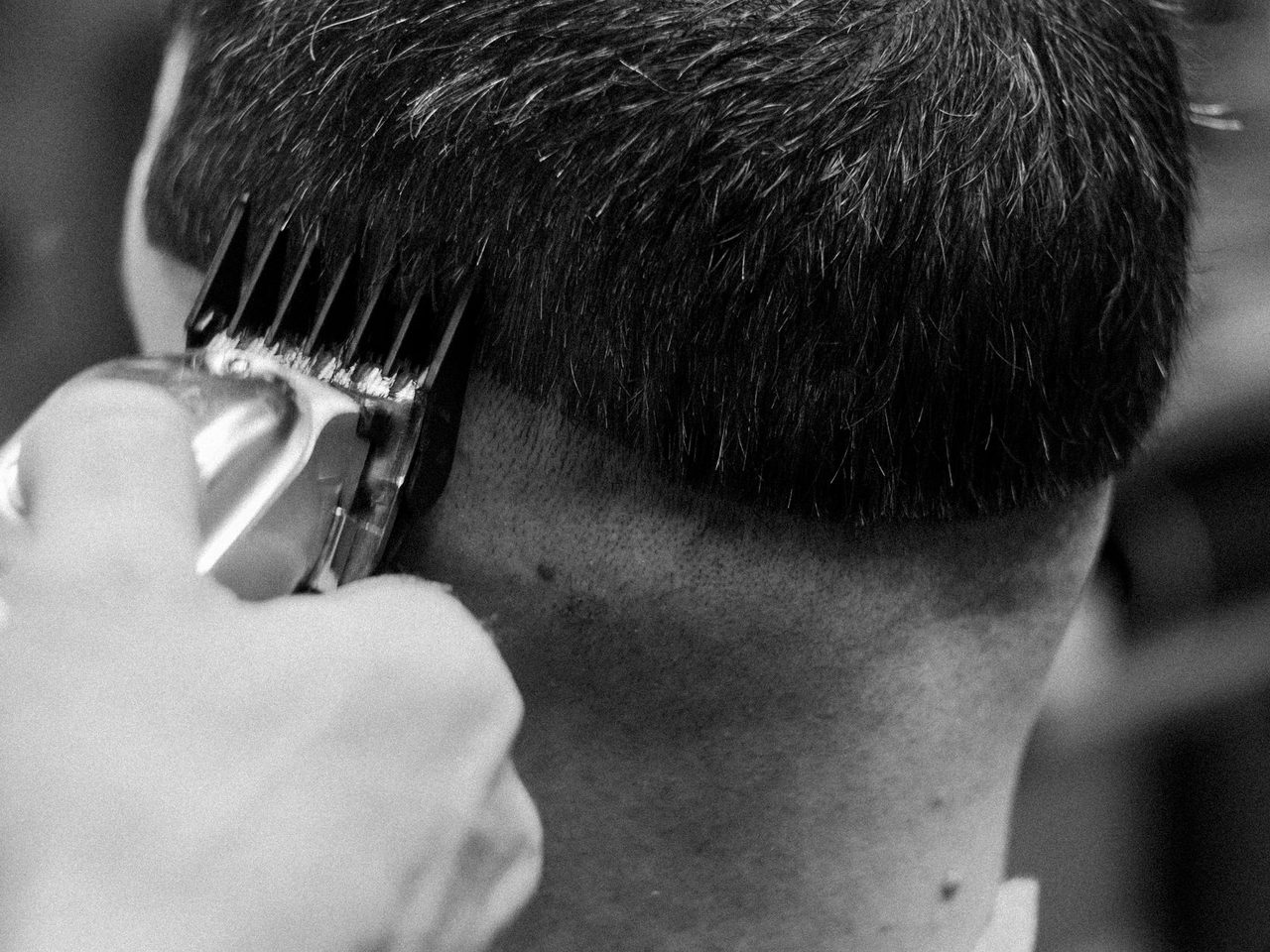 Black and white close-up of clippers trimming the back of a man's short dark hair