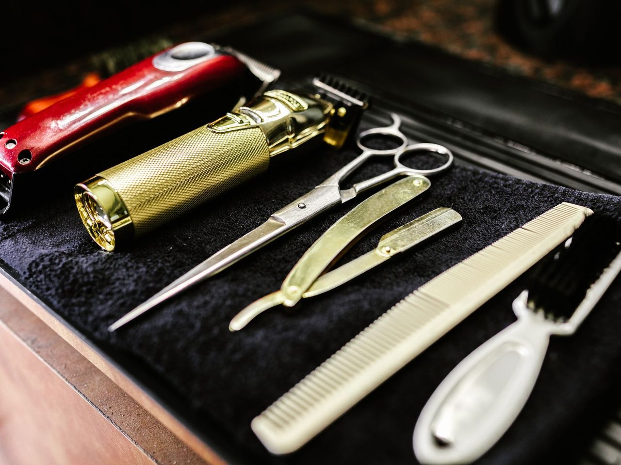 Hair clippers, scissors, razors and combs laid neatly on a black towel