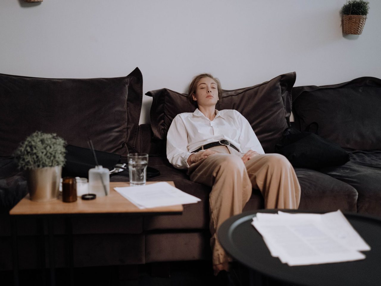 A woman sitting tiredly on a dark leather couch in a living room