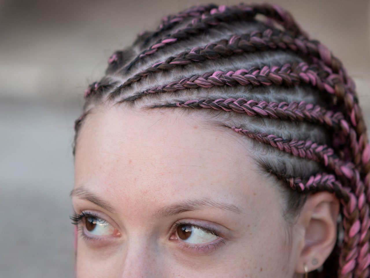 A woman with tight pink and brown cornrow braids running back from her hairline